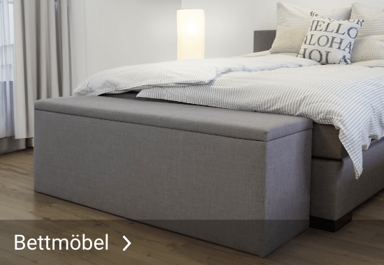 Grau gepolsterte Bettbank am Fußende eines Bettes mit gestreifter Bettwäsche und dem Text 'Bettmöbel'