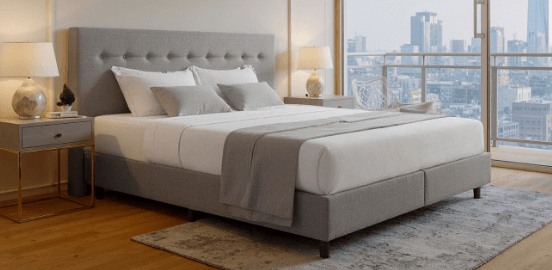Modernes Schlafzimmer mit grauem Polsterbett und ergonomischer Matratze, große Fenster mit Stadtblick