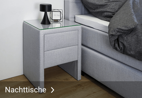 Grauer Nachttisch mit zwei Schubladen und Glasplatte neben einem grauen Bett mit dunkler Bettdecke und dem Text 'Nachttische'